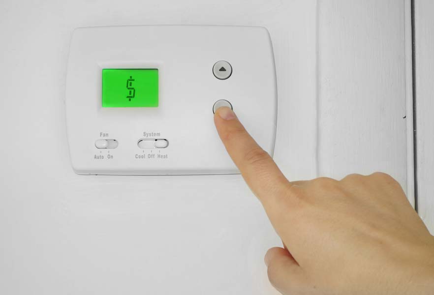 Person adjusting a wall thermostat with dollar sign symbol on the display.